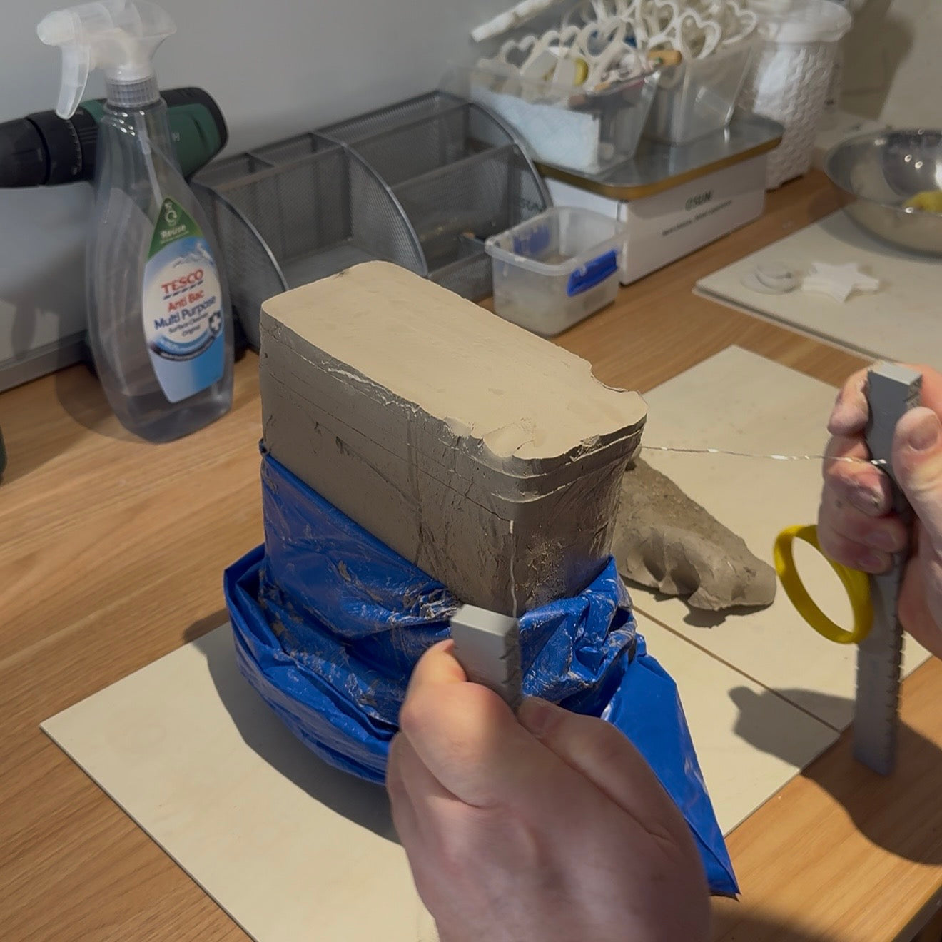 Hands slicing a block of clay with wire on a worktable for handmade ceramic keepsakes