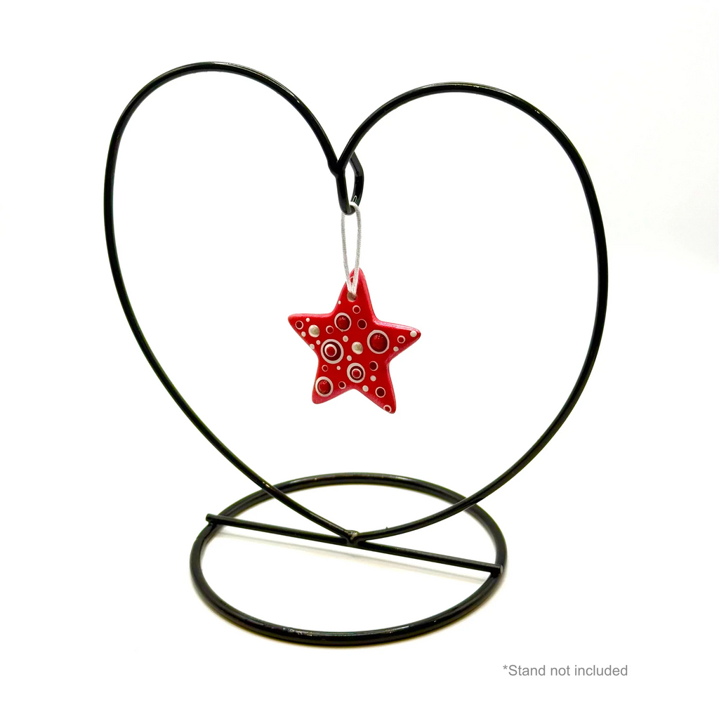 Red handmade ceramic star ornament with white dotted pattern, hanging on heart-shaped metal stand